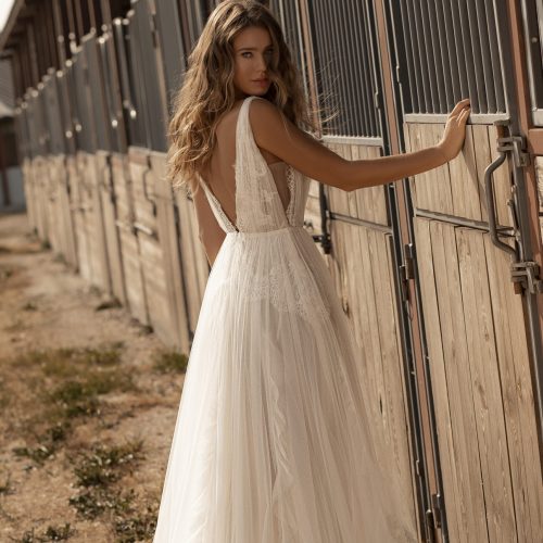 Eine Frau in einem weißen Hochzeitskleid mit Spitzenbesatz steht vor den hölzernen Stalltüren und blickt über ihre Schulter - sie fängt die Eleganz des Brautateliers bei Dornröschen in Nürnberg ein.