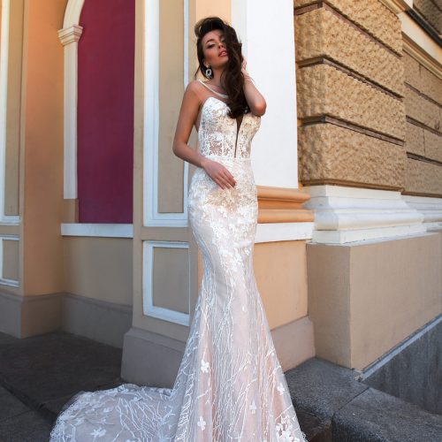 Eine Frau in einem trägerlosen Meerjungfrauen-Hochzeitskleid aus Spitze steht vor einem verschnörkelten Gebäude mit hohen Säulen und Bögen und präsentiert elegante Brautmode aus einem renommierten Brautatelier in Nürnberg.
