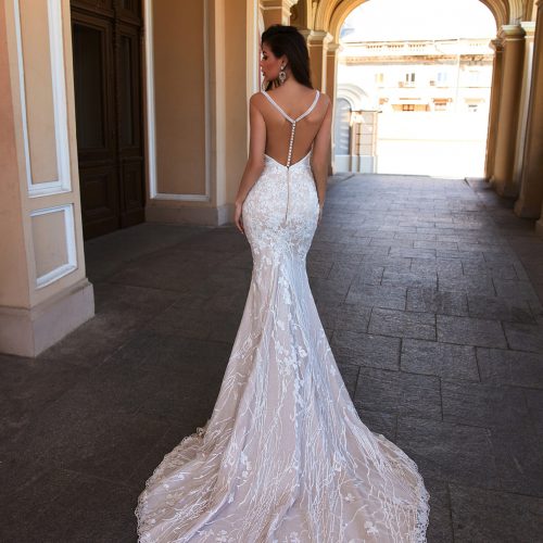 Eine Frau in einem weißen Spitzenhochzeitskleid mit langer Schleppe steht in einem bogenförmigen Durchgang, den Blick abgewandt - ein herrliches Beispiel für Brautmode aus einem Nürnberger Brautatelier.