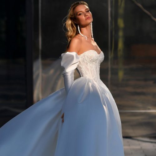 Eine Frau in einem weißen, schulterfreien Hochzeitskleid aus dem Brautatelier bei Dornröschen posiert im Freien im weichen Sonnenlicht.